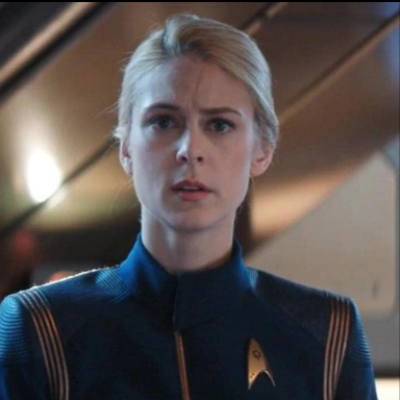 Photo of Sara Mitich during a scene of Star Trek: Discovery in  Lt. Nilsson costume wearing blue suit